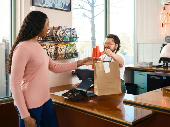 Customer receives a takeout bag from cashier.